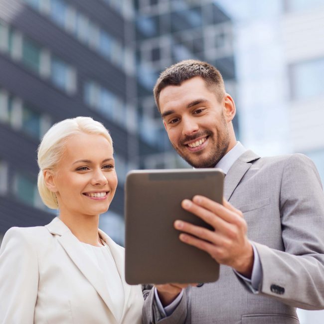 business, partnership, technology and people concept - smiling businessman and businesswoman with tablet pc computer over office building